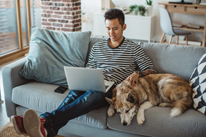man sitting on couch on laptop next to dog
